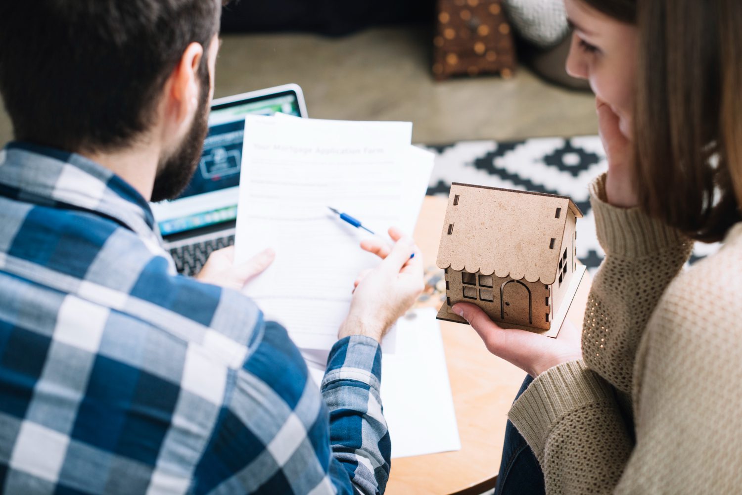 Couple Reviewing Mortgage Agreement With A Miniature House Model, Discussing Home Purchase