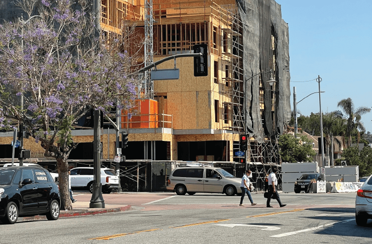 Urban Construction Site With A Partially Built Wooden Structure And Pedestrians Crossing The Street